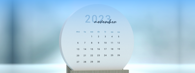 Round calendar showing November 2023. Days of the week are abbreviated in lowercase, set against a blurred blue background.