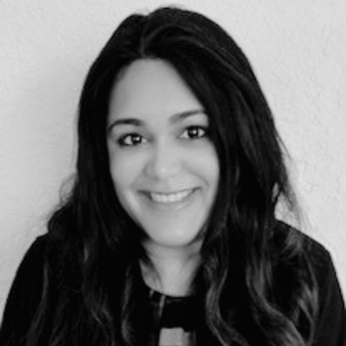 Smiling woman with long, dark hair against a light background. She's wearing a dark top, and the photo is in black and white, conveying a friendly tone.